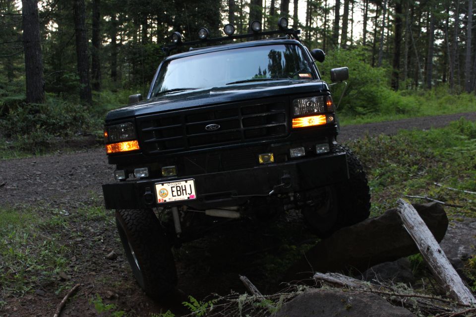 Black Ford Bronco on a dirt path with trees around it. License plate reads EBHJ