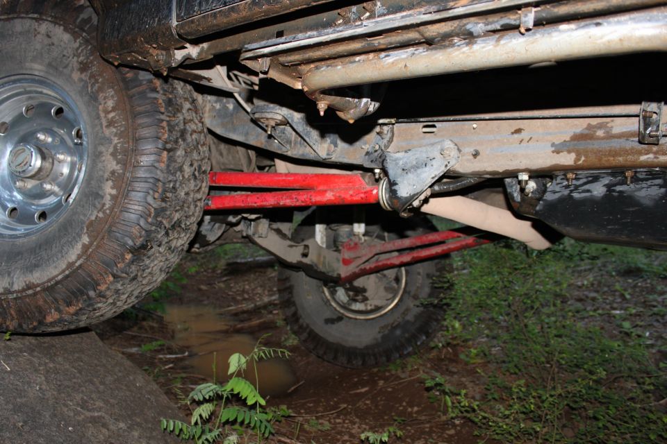 Undercarriage of a muddy off-road vehicle with red suspension components and large tires on uneven terrain