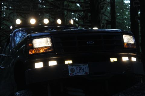 1995 Ford Bronco - A dark Ford truck with multiple lights illuminates the forest at night.