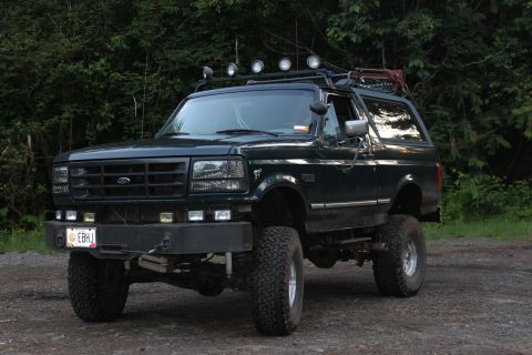 1995 Ford Bronco - This lifted Ford Bronco is parked on a dirt road with trees in the background.