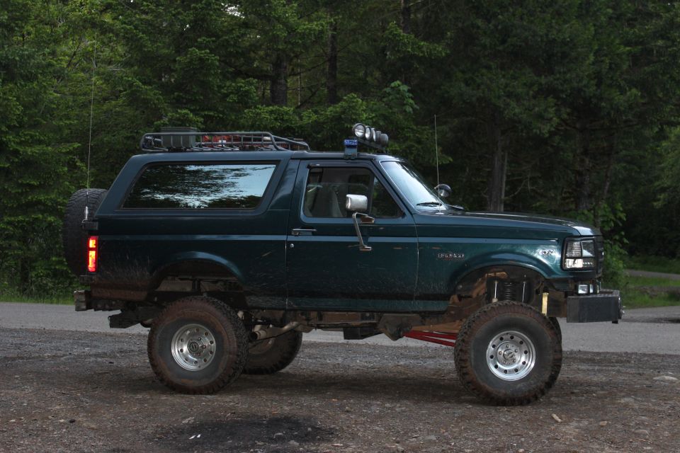 Dark green 1995 Ford Bronco with roof rack and off-road tires parked on dirt