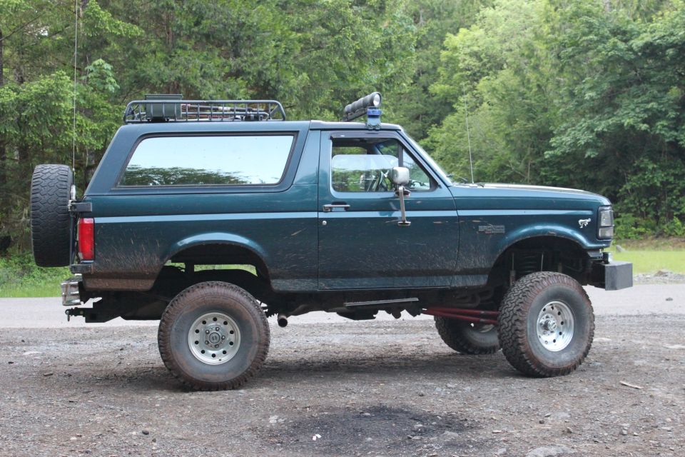 Dark green Ford Bronco, lifted, with roof rack and spare tire, parked on dirt road