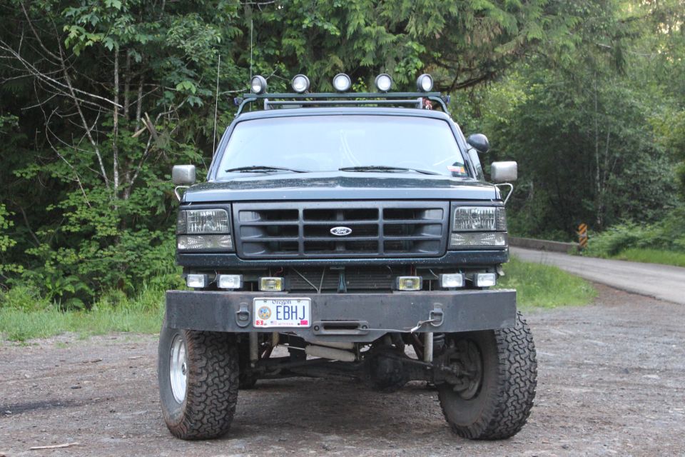 Front view of a dark green Ford Bronco with a large aftermarket bumper and roof lights. License plate reads EBHJ