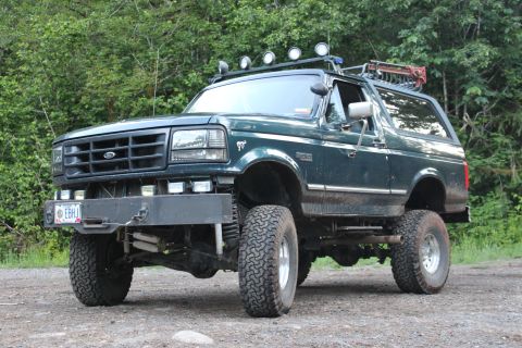 1995 Ford Bronco - This lifted Ford Bronco is parked on a dirt road with trees in the background.