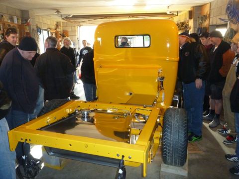 1969 Lincoln Continental - A group of people observe the chassis of a bright yellow pickup truck during a gathering.