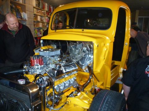 1969 Lincoln Continental - A bright yellow hot rod truck is shown with its hood open, revealing a highly polished chrome engine. Several people are observing the vehi…