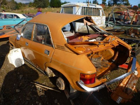 1969 Lincoln Continental - This heavily damaged orange sedan sits in a junkyard, with its rear end open and rusted.