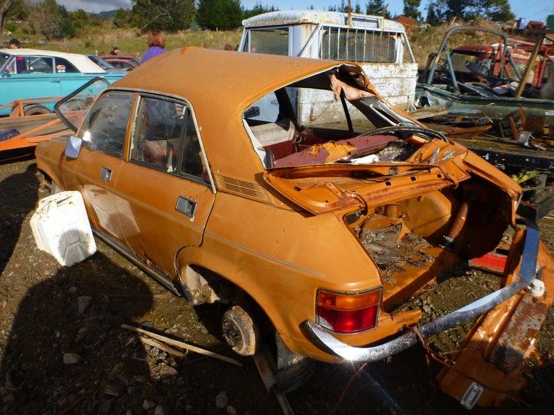 Wrecked orange sedan, rear view, in junkyard