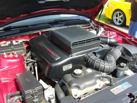 2007 Ford Mustang - The engine bay of a 2007 Ford Mustang, a 'Ford Racing' cover and 'Shaker' branding, with another Mustang visible in the background.