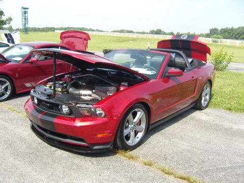 2007 Ford Mustang - Two red Mustangs are parked outside with their hoods open, displaying their engines on a sunny day.
