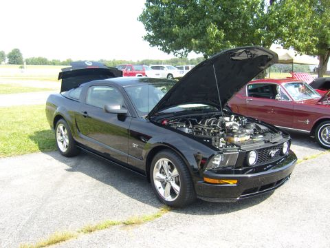2007 Ford Mustang - A black Ford Mustang GT is displayed with its hood and trunk open, alongside another classic car.