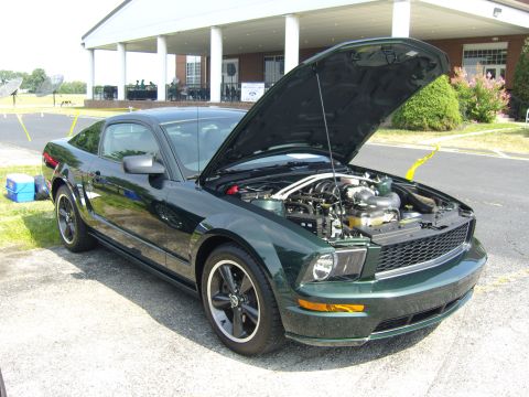 2007 Ford Mustang - Dark green 2007 Ford Mustang coupe with hood open, parked on pavement near a building.