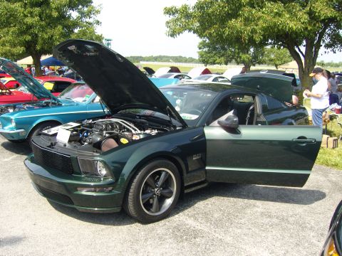 2007 Ford Mustang - A dark green Ford Mustang is displayed with its hood and door open at an outdoor car show.