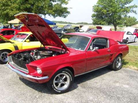 2007 Ford Mustang - A classic red Ford Mustang coupe is displayed with its hood open, revealing the engine bay. Other vehicles are visible in the background at…
