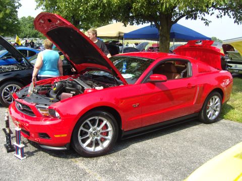 2007 Ford Mustang - A red Ford Mustang GT is displayed with its hood and trunk open at an outdoor event, with trophies nearby.