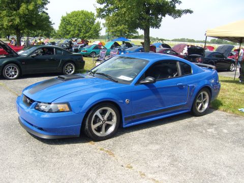 2007 Ford Mustang - A blue 2007 Ford Mustang coupe with black racing stripes is parked at an outdoor car show.