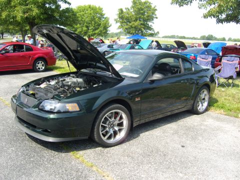 2007 Ford Mustang - Dark green Ford Mustang parked outdoors with hood open, other vehicles visible.