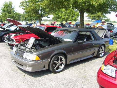 2007 Ford Mustang - A gray convertible Mustang is displayed with its hood open at an outdoor car show, alongside other vehicles.