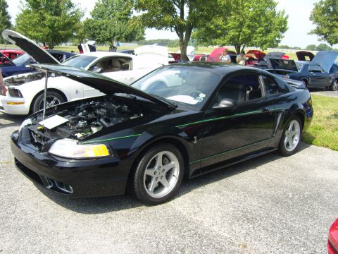 2007 Ford Mustang - Black Ford Mustang with green stripe, hood open, parked at an outdoor car show.