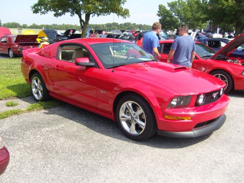 2007 Ford Mustang - A red Ford Mustang GT is displayed at a car show, with other vehicles in the background.