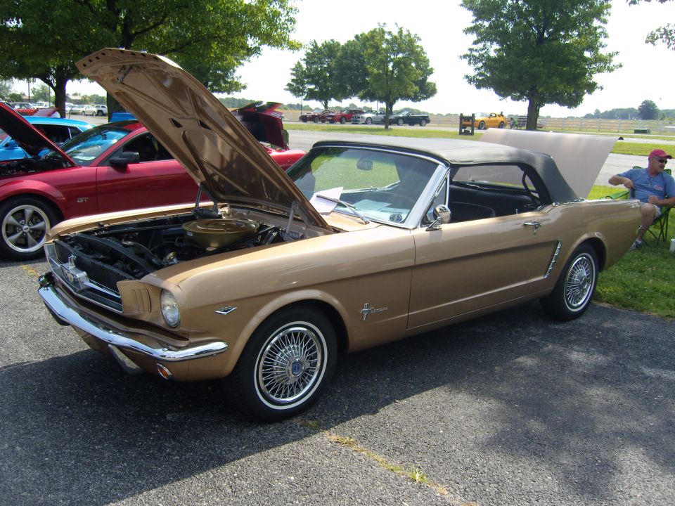 Gold 1965 Ford Mustang convertible with hood open, parked next to a red Mustang