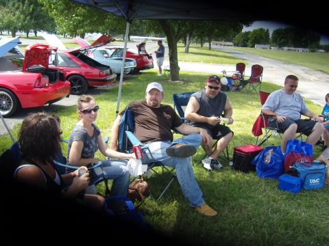 2007 Ford Mustang - Several people relax in lawn chairs under a tent, with a line of Mustangs parked behind them.