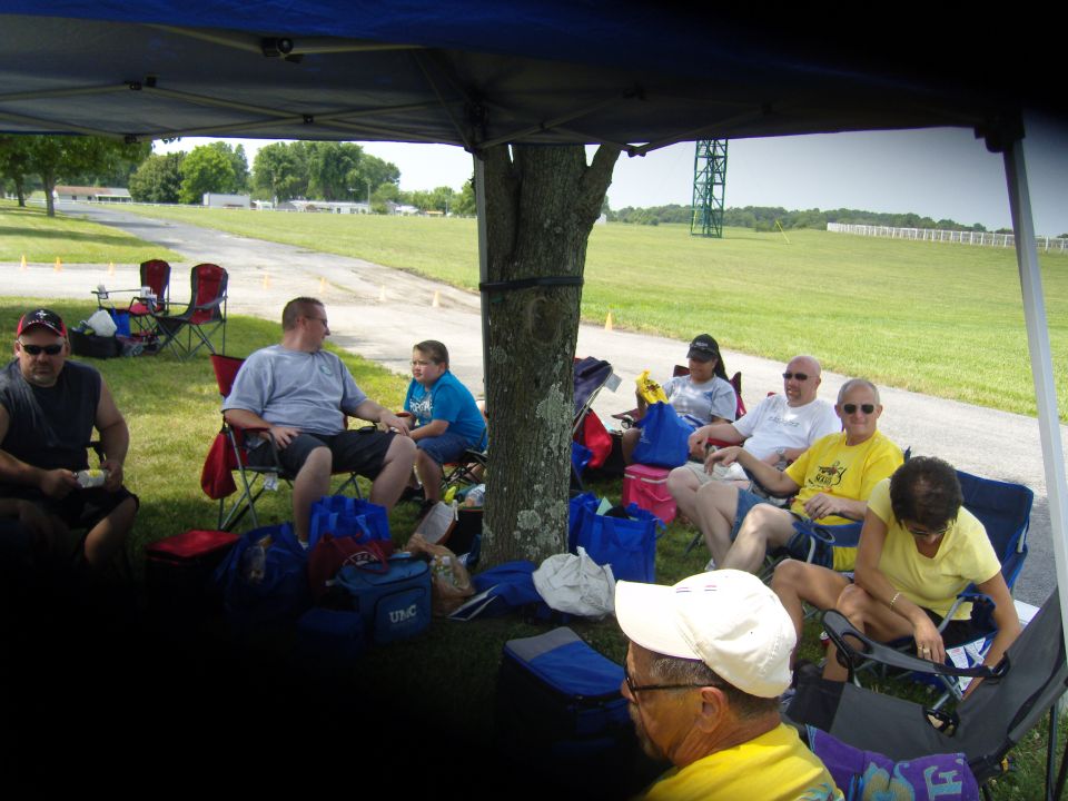 People gathered under a blue canopy at an outdoor event