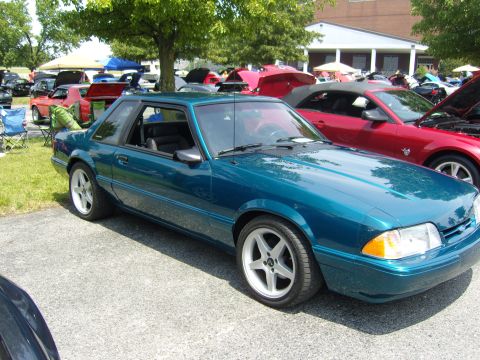 2007 Ford Mustang - Teal coupe with aftermarket wheels at a car show, other vehicles present.
