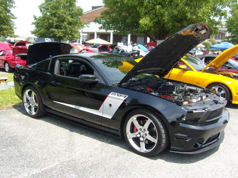 2007 Ford Mustang - A black 2007 Ford Mustang is displayed with its hood open, alongside other vehicles at an outdoor event.
