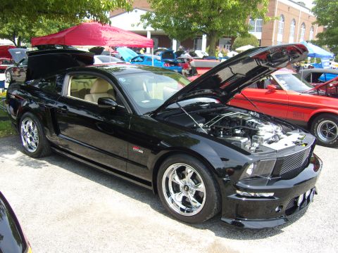 2007 Ford Mustang - A black 2007 Ford Mustang is displayed with its hood open, revealing the engine bay, at an outdoor car show.