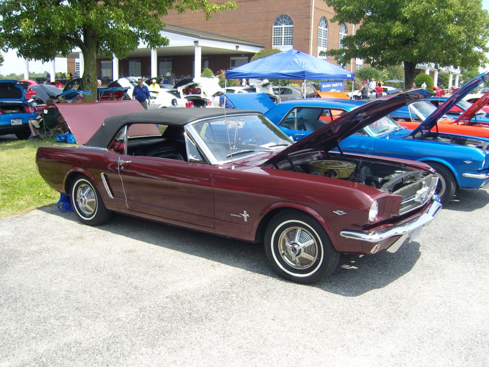 Maroon convertible with hood open, parked in front of a building with other cars