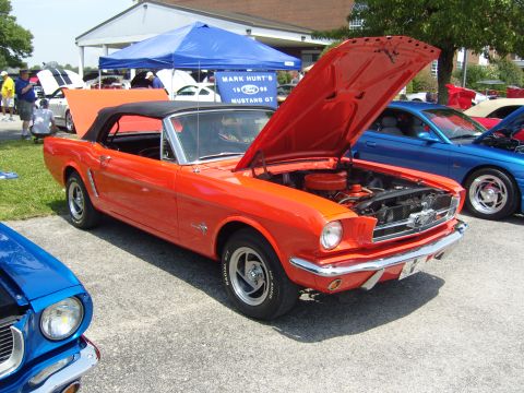 2007 Ford Mustang - A classic orange Ford Mustang convertible is displayed with its hood open at an outdoor car show.