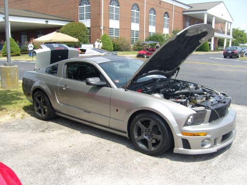 2007 Ford Mustang - A silver Ford Mustang is parked outside a building with its hood open, revealing the engine compartment.