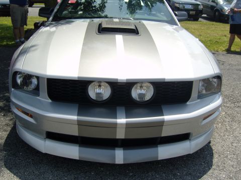 2007 Ford Mustang - A silver Ford Mustang with racing stripes is parked outdoors, showing its front grille and headlights.