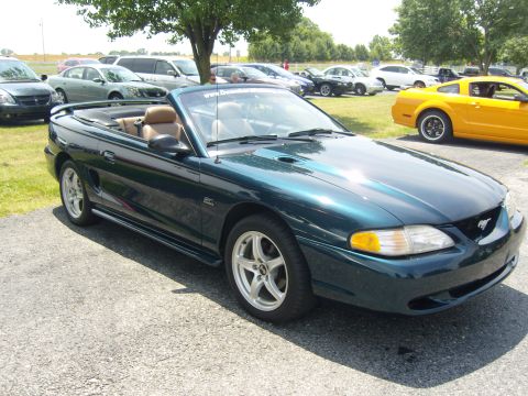 2007 Ford Mustang - This dark green 1994 Ford Mustang convertible is parked on asphalt with other vehicles in the background.
