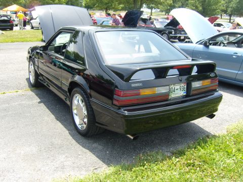 2007 Ford Mustang - Black coupe at car show, hood open, parked on asphalt with grass nearby.