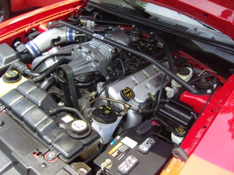 2007 Ford Mustang - The engine bay of a red Ford Mustang shows a V8 32 valve engine with a supercharger and custom intake.