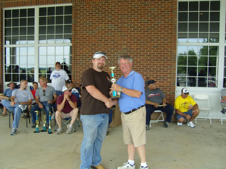 Two men shaking hands over a trophy at an outdoor event