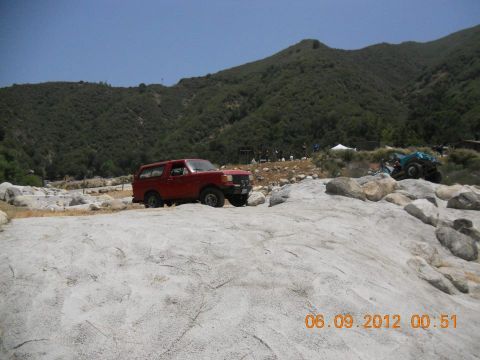 1988 Ford Bronco - A red 1987 Ford Bronco navigates a rocky terrain with a mountain range behind it.