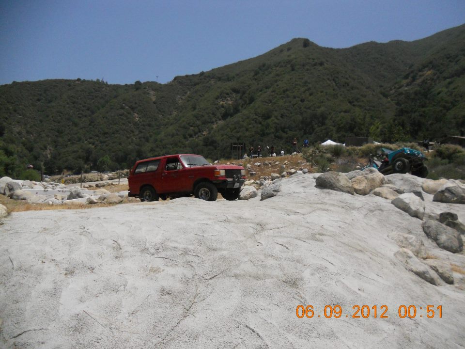 Red 1987 Ford Bronco parked on a rocky incline with a mountain in the background