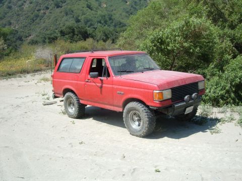 1988 Ford Bronco - This red SUV, likely a 1987 model, is parked off-road with its front end angled towards the camera.