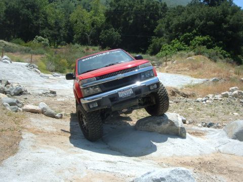 1988 Ford Bronco - Red Chevrolet Colorado pickup truck navigating rocky terrain on an off-road trail.