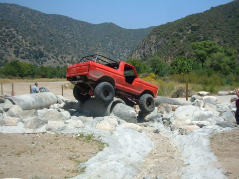 1988 Ford Bronco - This red SUV is navigating a challenging obstacle course with large rocks and concrete pipes.