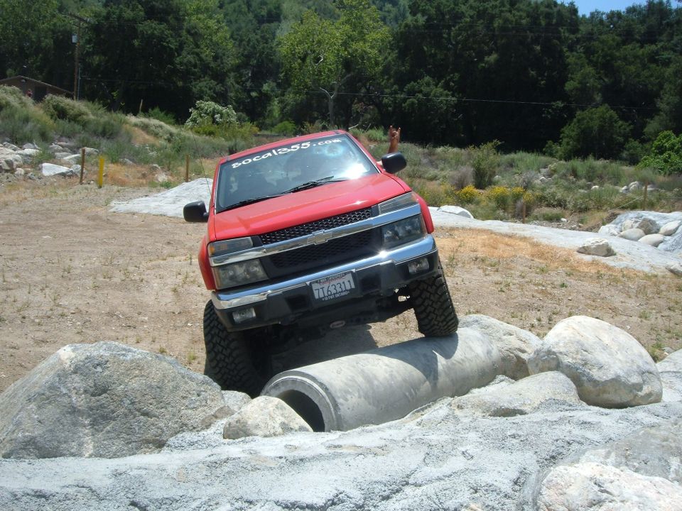 Red pickup truck with lifted suspension driving over concrete pipe and rocks