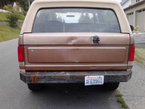 1989 Ford Bronco - Rear view of a 1989 Ford Bronco, a dented tailgate and a custom bumper.
