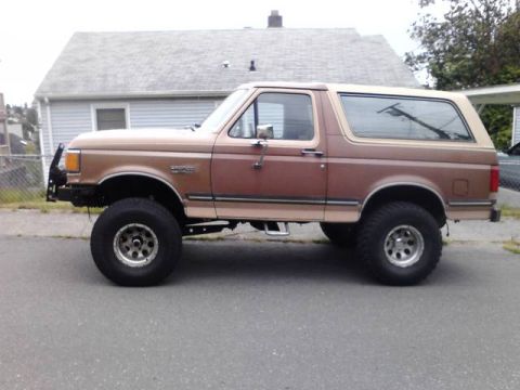 1989 Ford Bronco - Side profile of a lifted 1989 Ford Bronco with a custom front bumper and removable tan top.