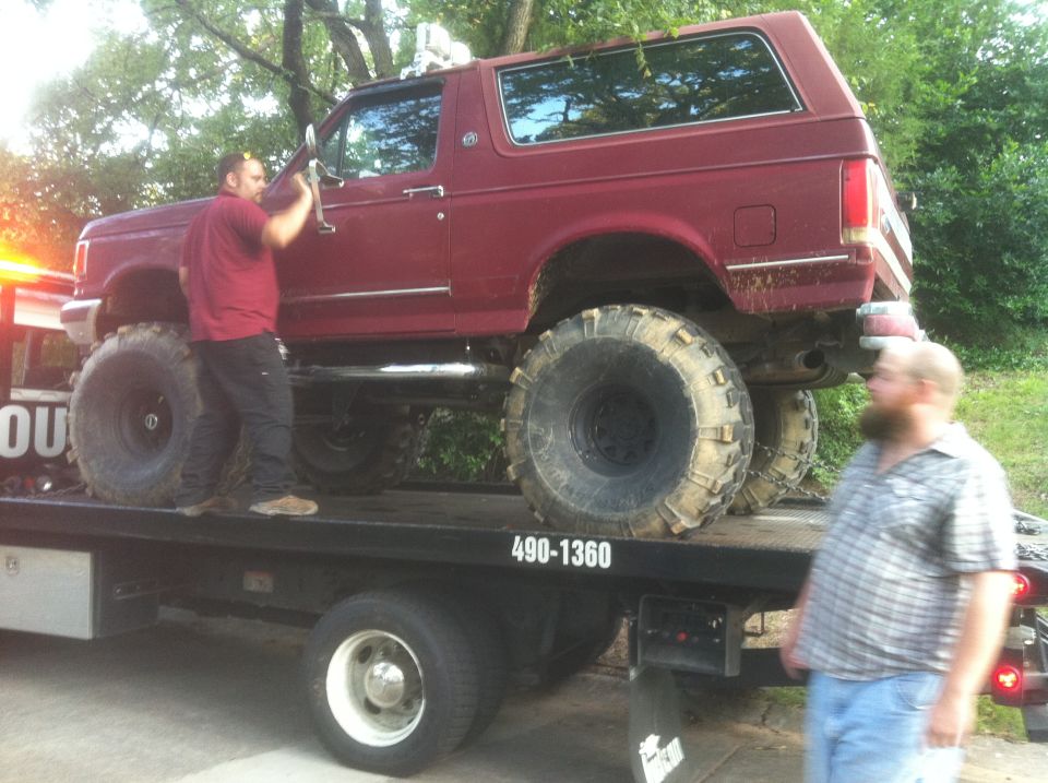 Red Ford Bronco with oversized tires on a flatbed tow truck