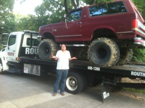 1991 Ford Bronco - A lifted 1991 Ford Bronco is being transported on a tow truck, with a person standing beside it.
