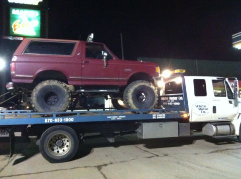 1991 Ford Bronco - A lifted red Ford Bronco is transported on a tow truck at night.