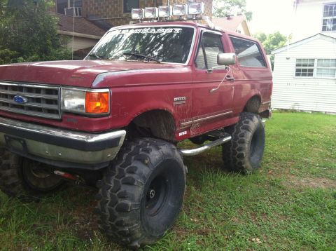 1991 Ford Bronco - Modified 1991 Ford Bronco with oversized tires and roof-mounted light bar parked on grass.